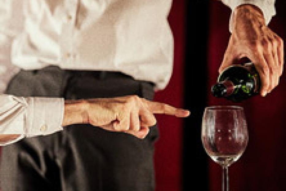 Eine Person gießt Wein in ein Glas, während sie mit dem Finger darauf zeigt.
