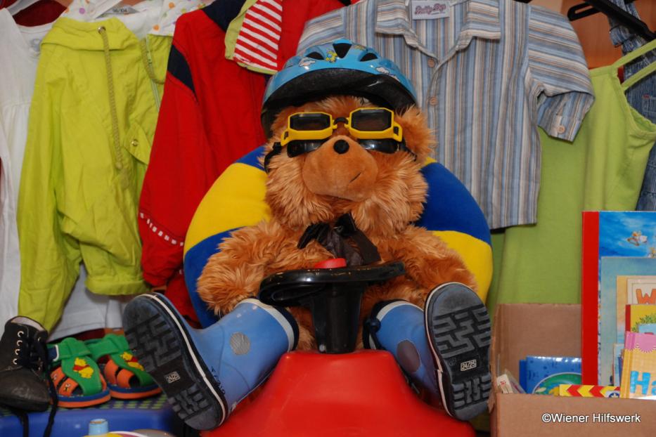 Ein Teddybär mit Helm und Brille sitzt auf einem roten Spielzeugauto.