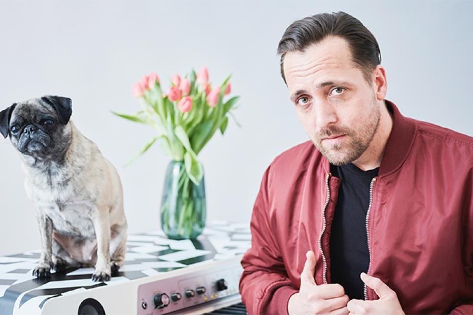 Ein Mann mit Mops und Tulpen vor einem Klavier.