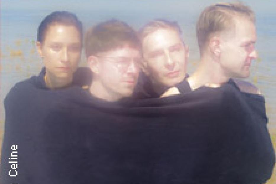 Vier Personen stehen am Wasser und sind in ein schwarzes Tuch gehüllt.