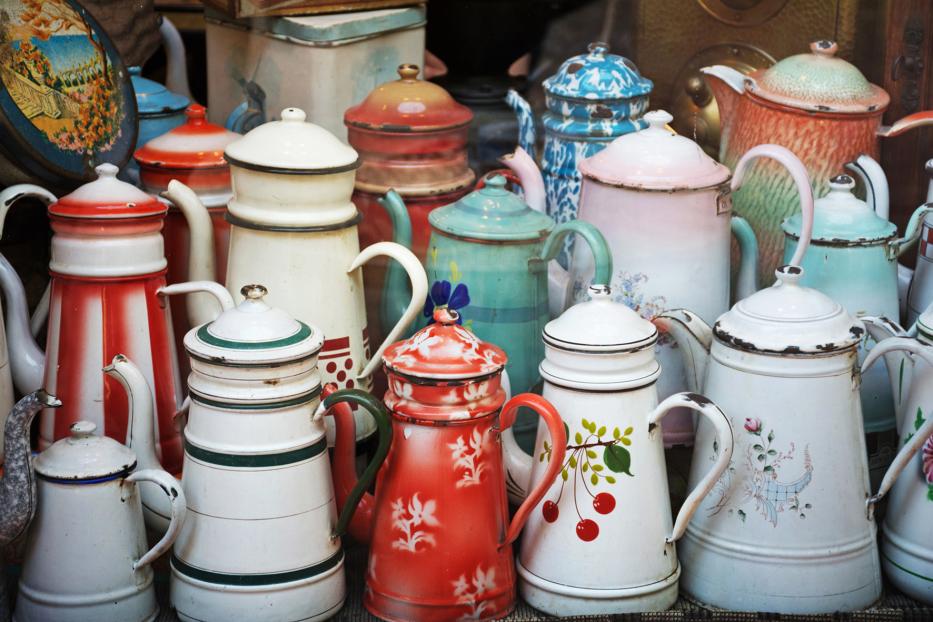 Eine Sammlung von alten, bunten Emaille-Kaffeekannen steht nebeneinander.