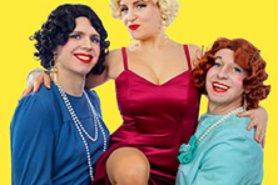 Drei als Frauen verkleidete Personen posieren vor einem gelben Hintergrund.