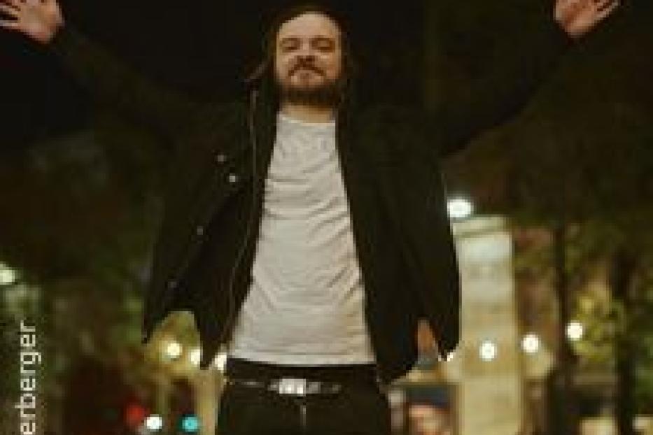 Ein Mann mit Bart steht nachts mit ausgebreiteten Armen auf der Straße.