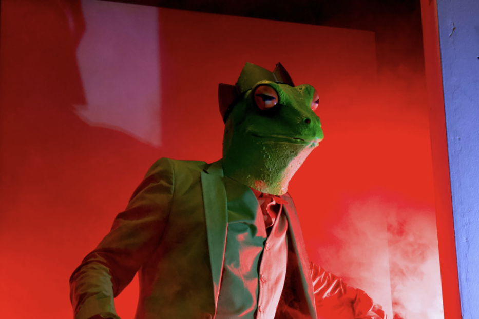 Ein Frosch mit Anzug und Hut steht unter einem Bitcoin-Symbol.