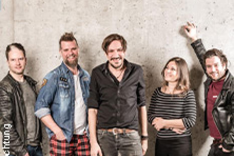 Eine Band posiert vor einer grauen Wand für ein Gruppenfoto.