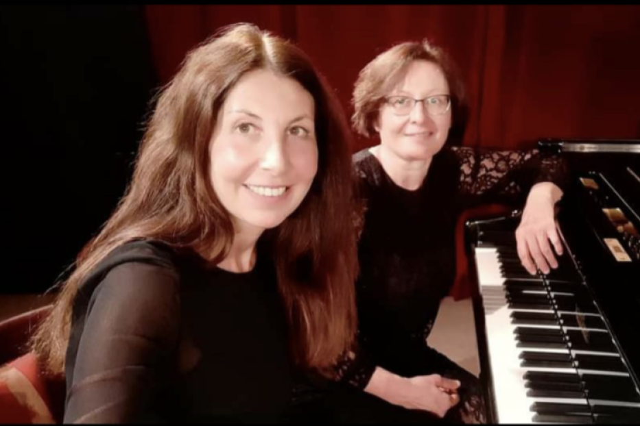 Zwei Frauen sitzen an einem Klavier und lächeln.