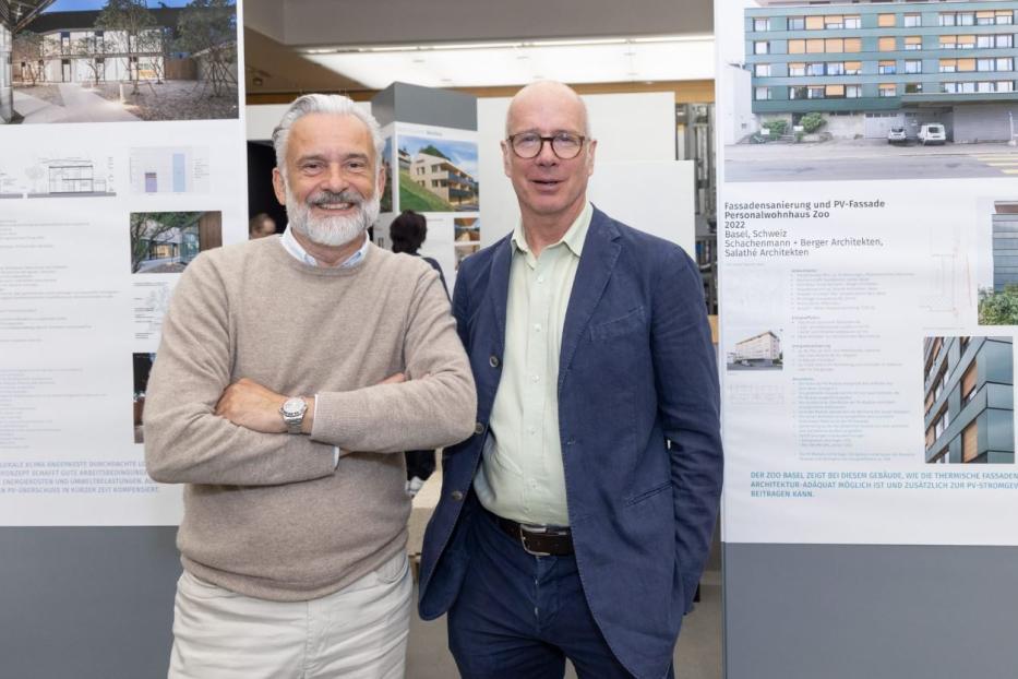 Zwei Männer stehen vor Plakaten, die ein architektonisches Projekt zeigen.