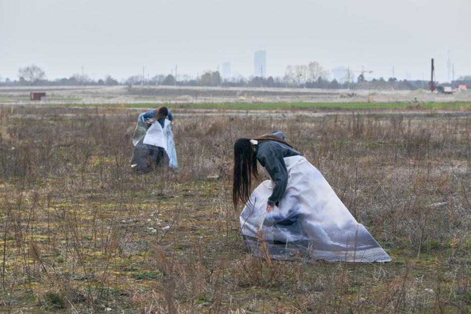 Zwei Frauen in Kleidern mit Landschaftsmotiven stehen auf einem Feld.