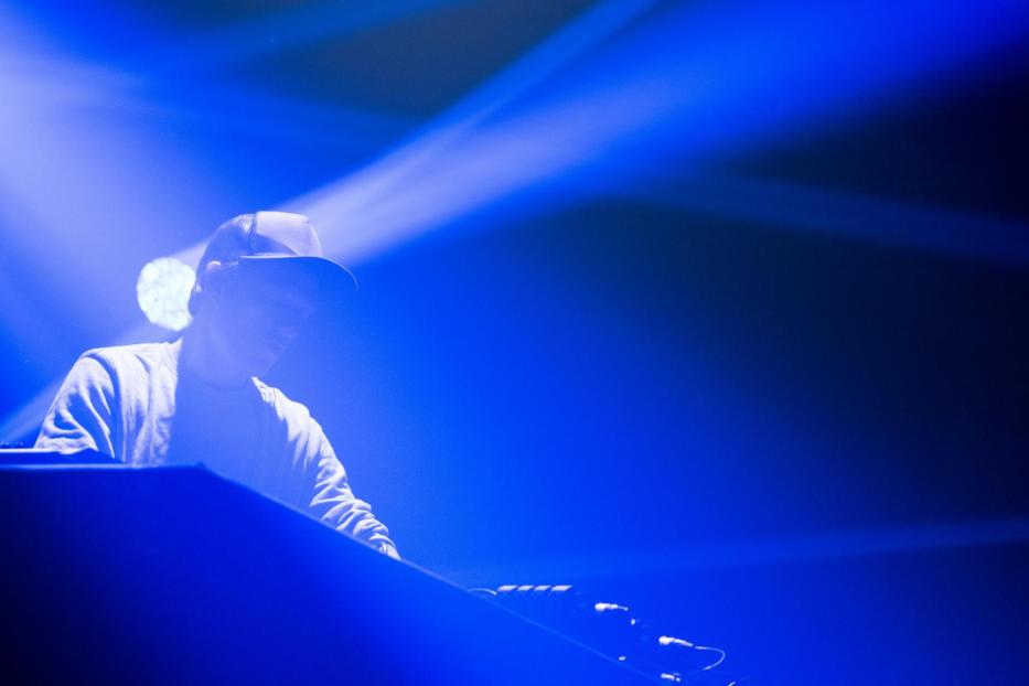 Ein DJ mit Kappe legt unter blauem Licht Musik auf.