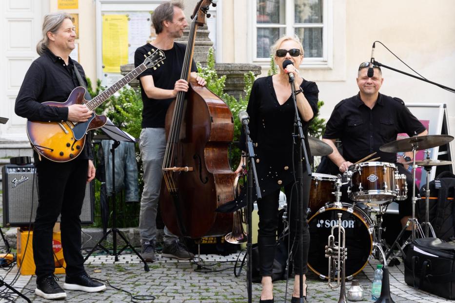 Eine Jazzband spielt im Freien mit Sängerin, Gitarrist, Bassist und Schlagzeuger.