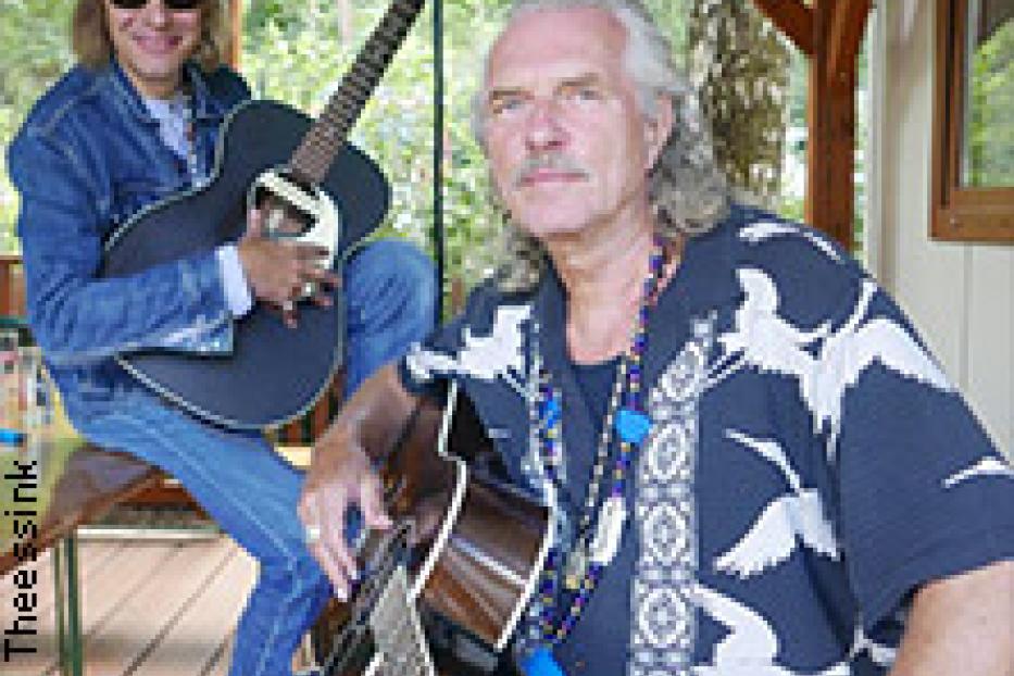 Zwei Musiker, der eine mit Hut und Sonnenbrille, posieren mit ihren Gitarren.