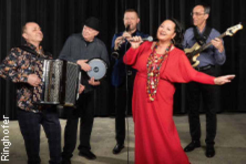Eine Band mit Sängerin, Akkordeon, Gitarre und Schlagzeug tritt auf einer Bühne auf.