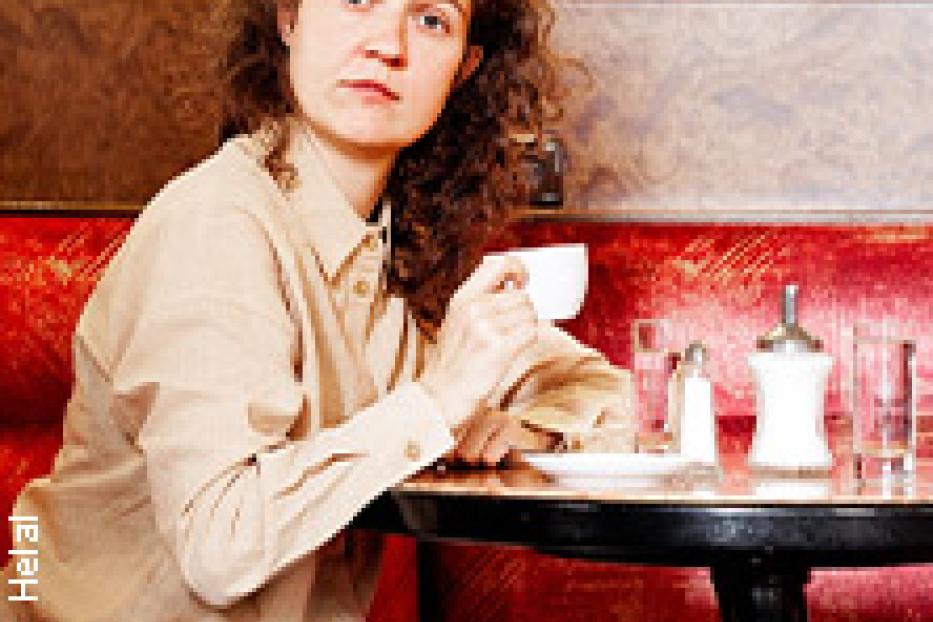 Eine Frau sitzt in einem Café und hält eine Tasse in der Hand.