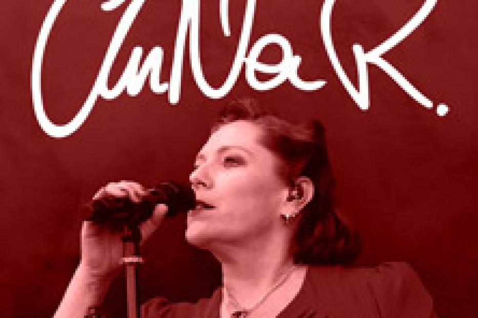 Anna R. singt mit Mikrofon vor einem roten Hintergrund, auf dem ihr Name steht.