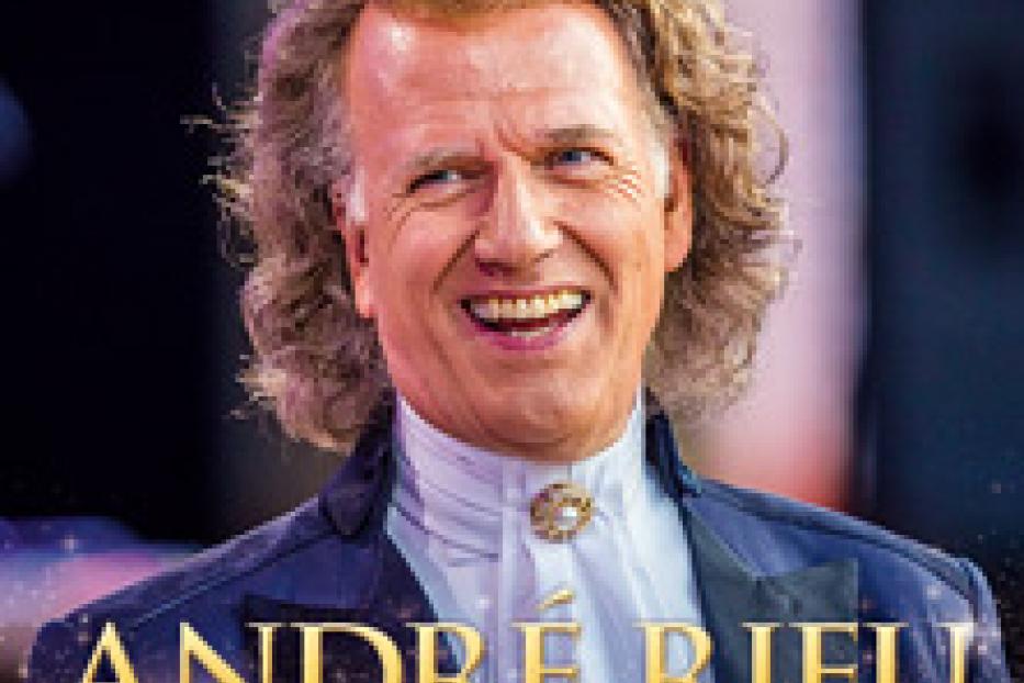 André Rieu lächelt in einem blauen Anzug vor einem verschwommenen Hintergrund.
