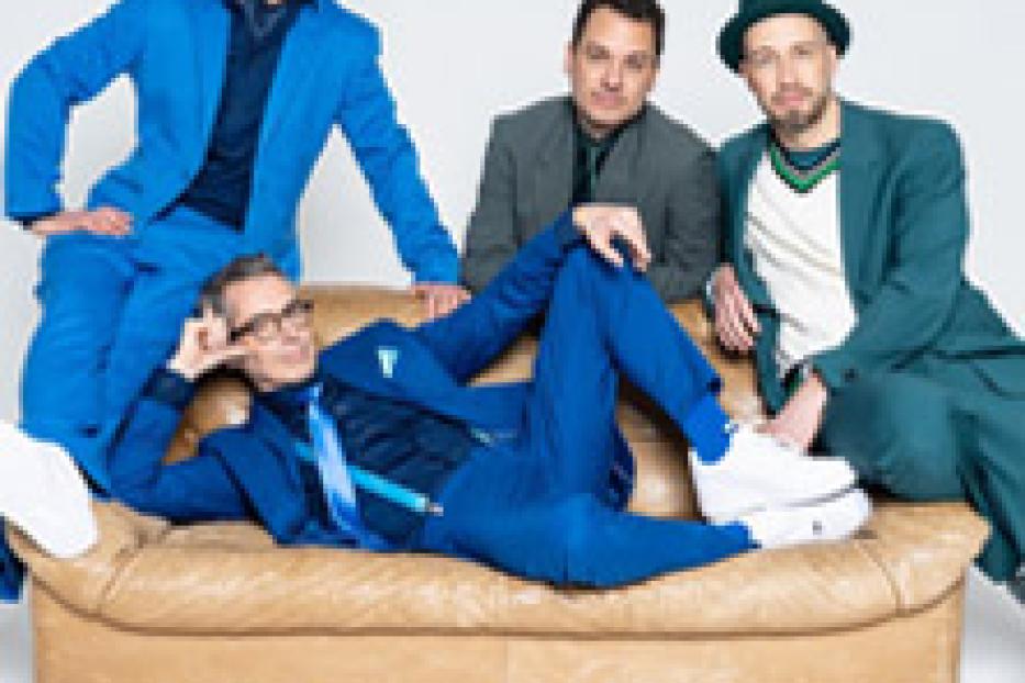 Die Fantastischen Vier posieren auf einem beigen Sofa.