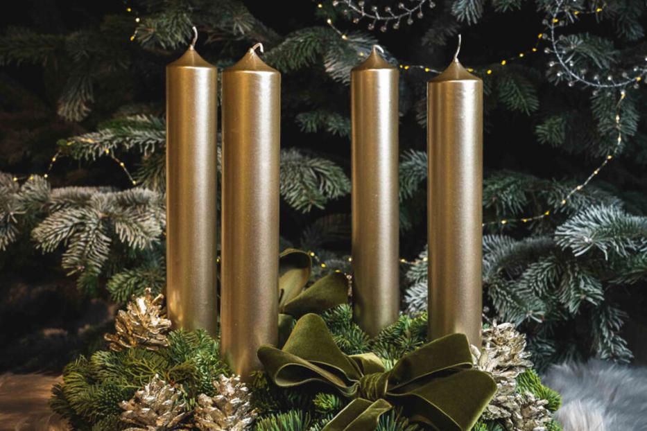 Ein Adventskranz mit vier goldenen Kerzen, Tannenzweigen, goldenen Zapfen und einer grünen Schleife.