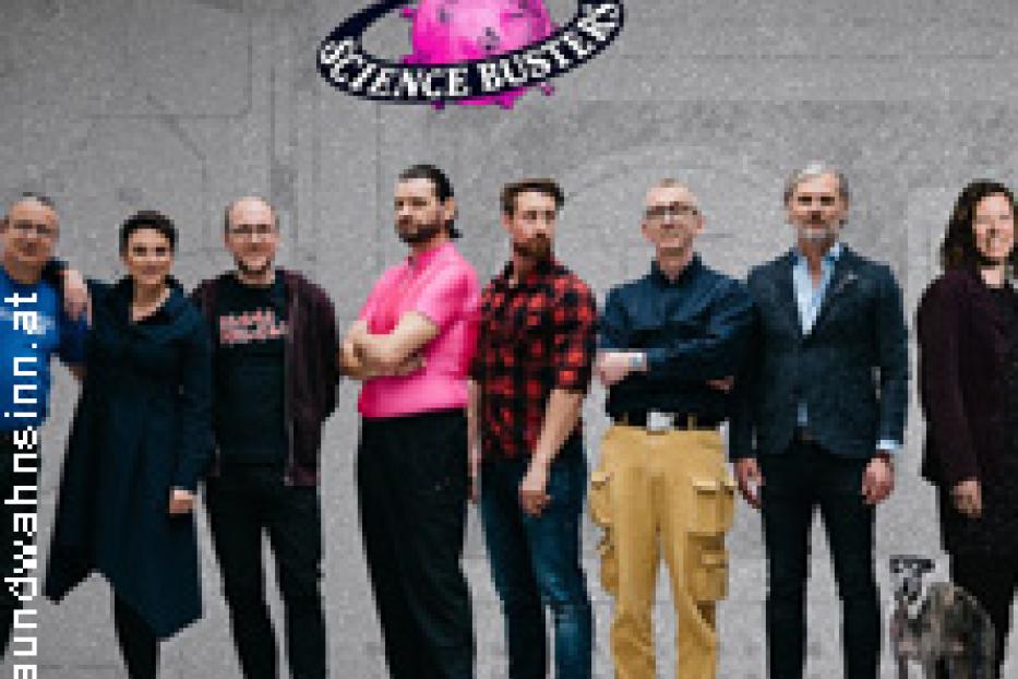 Die Science Busters posieren vor einer grauen Wand, ein Hund steht am Rand.