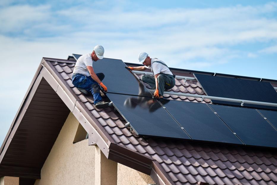 Arbeiter installieren Module für eine Photovoltaik-Anlage auf dem Dach eines Einfamilienhauses.
