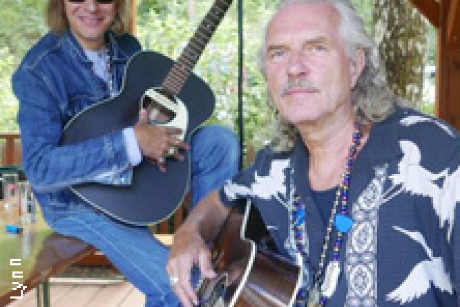 Zwei Männer mit Gitarren posieren für ein Foto im Freien.