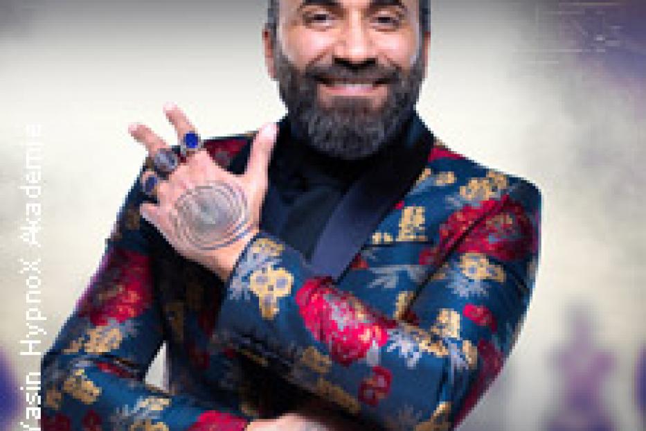 Ein Mann mit Bart und auffälligem Sakko lächelt in die Kamera.