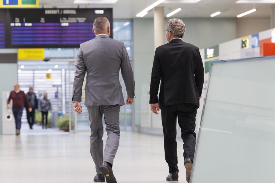 Landeshauptmann Mario Kunasek (FPÖ) (li.) und sein Vorgänger Christopher Drexler (ÖVP) (re.) sind von hinten zu sehen. Beide tragen Anzug und schreiten nebeneinander vom Betrachter weg.