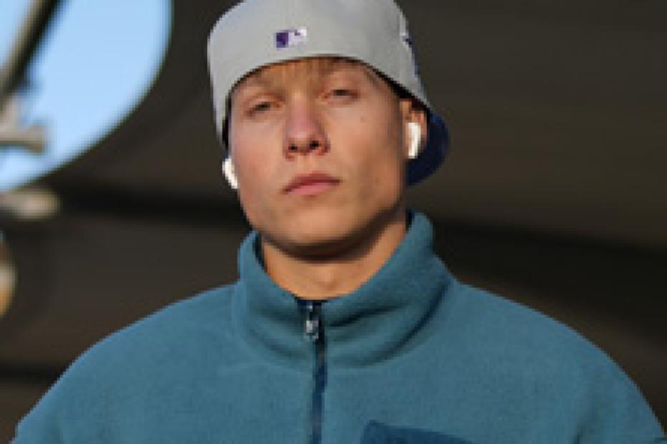 Ein junger Mann mit hellblondem Haar trägt eine graue Baseballkappe und eine blaue Fleecejacke.