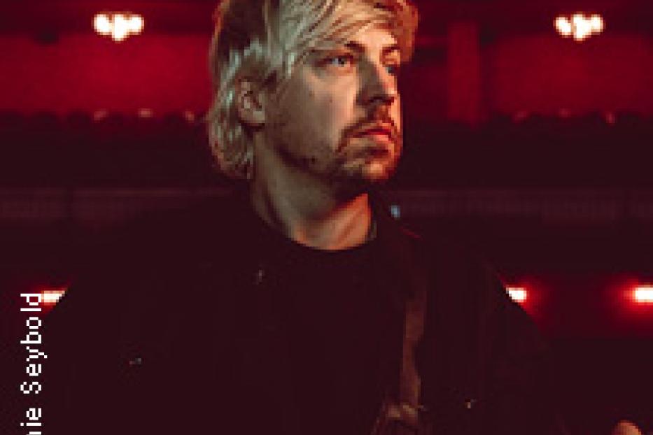 Ein Mann mit blonden Haaren und Bart hält eine Gitarre.