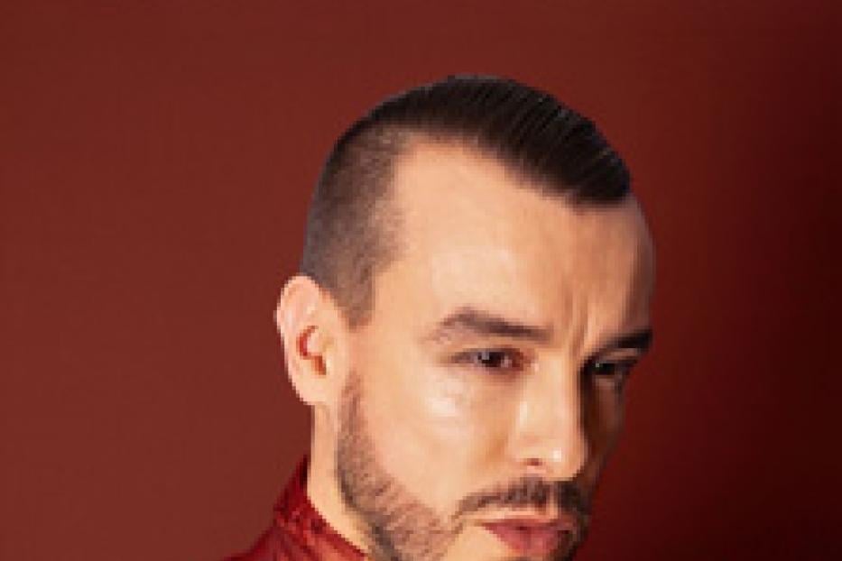 Ein Porträt von Cem Adrian vor einem roten Hintergrund.