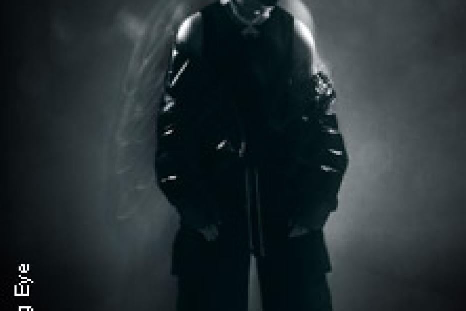 Ein Mann in dunkler Kleidung steht vor einem dunklen Hintergrund.