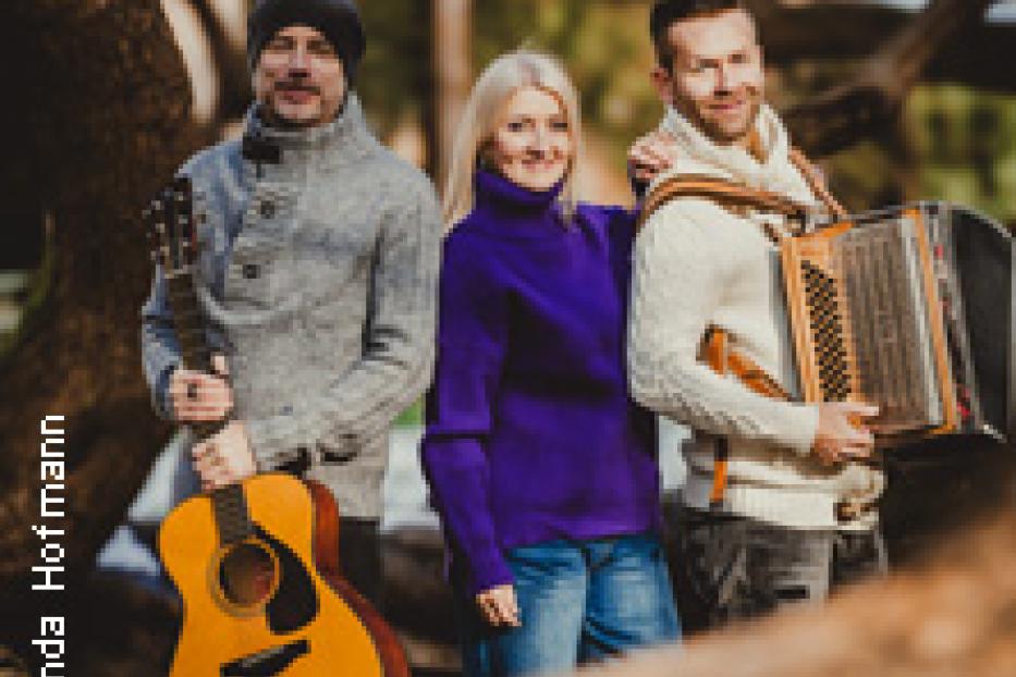 Eine Musikgruppe posiert mit Gitarre und Akkordeon im Wald.