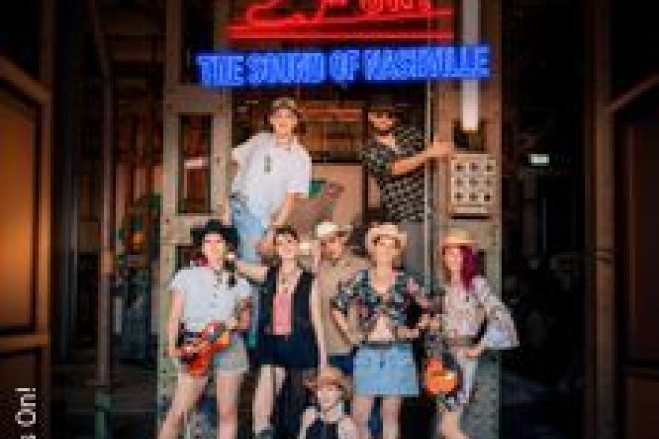 Eine Gruppe von Personen posiert vor einem Neonreklameschild mit der Aufschrift „Boots On! The Sound of Nashville“.