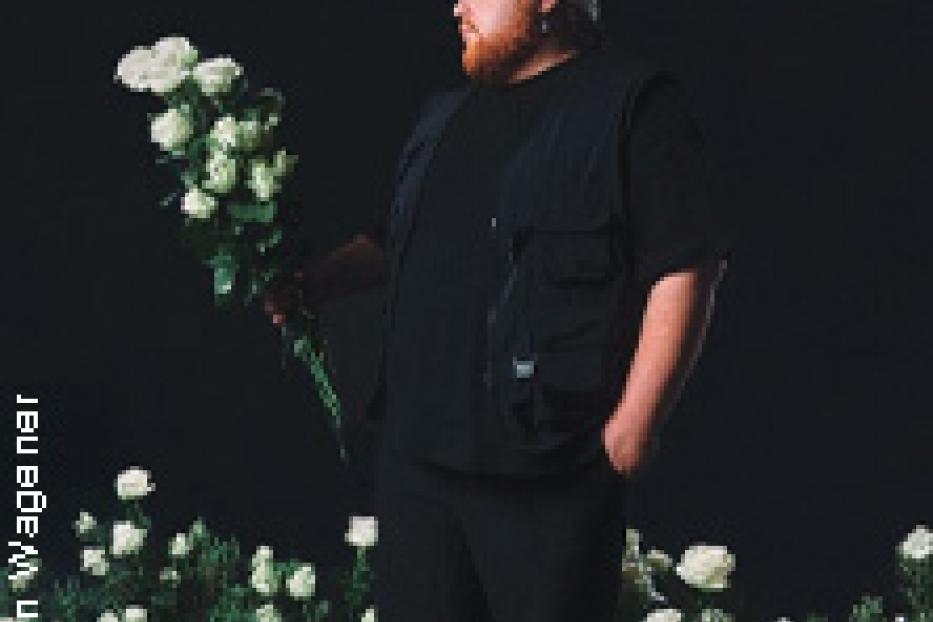 Ein Mann mit Bart und weißem Tuch hält einen Strauß weißer Rosen.