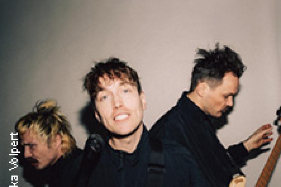 Eine Band spielt vor einer grauen Wand.