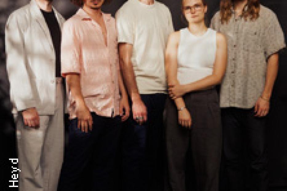 Fünf Bandmitglieder posieren vor einem dunklen Hintergrund.