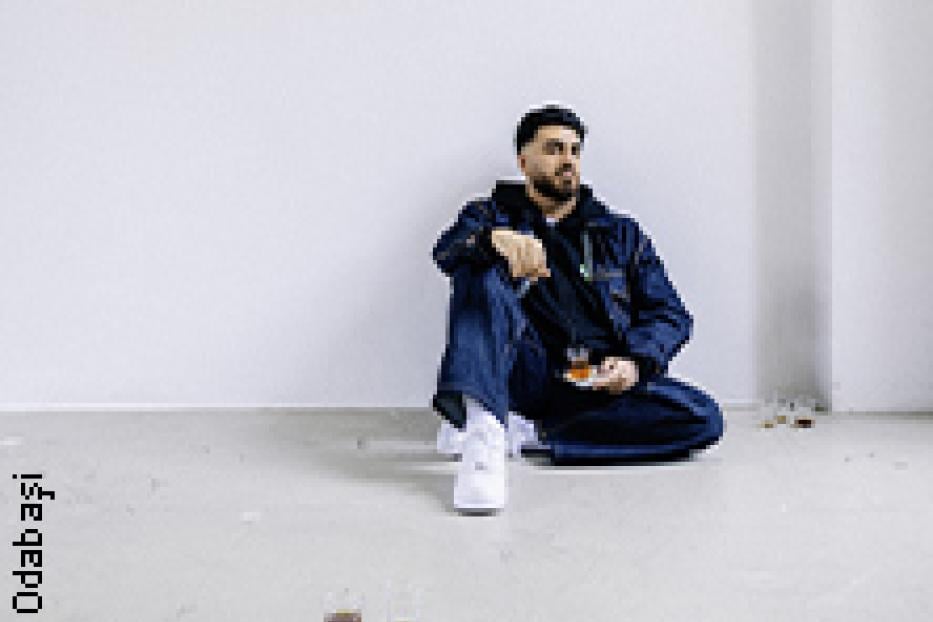 Ein Mann sitzt auf dem Boden in einem leeren Raum und hält ein Glas in der Hand.