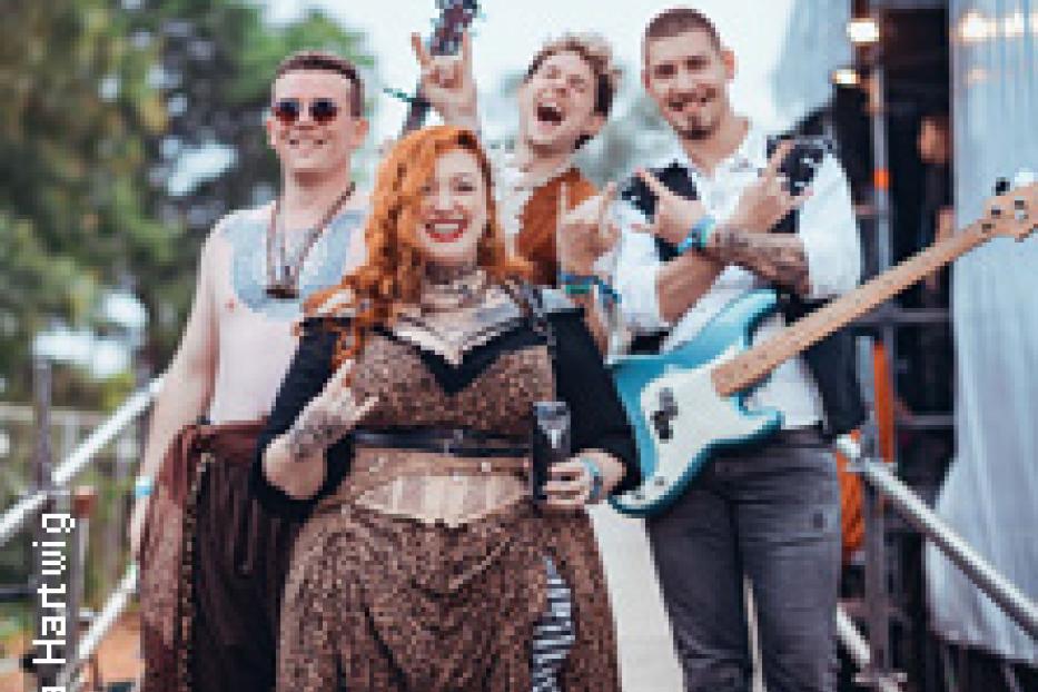 Eine Band posiert auf einer Treppe mit Instrumenten und ausgefallenen Kostümen.