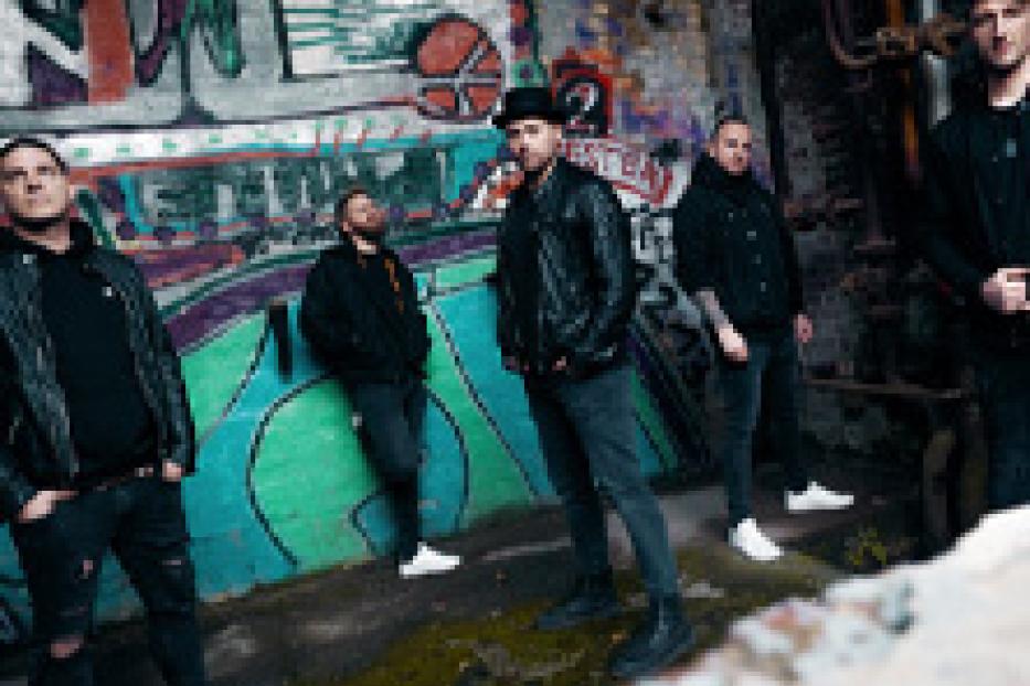 Eine Band posiert vor einer Wand mit Graffiti in einer städtischen Umgebung.