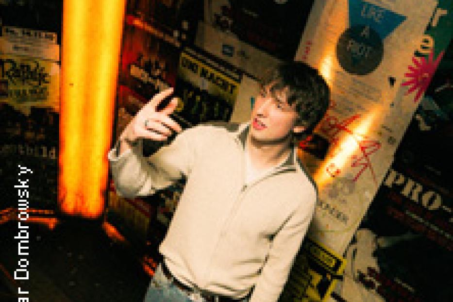 Ein junger Mann steht vor einer Wand voller Konzertplakate.