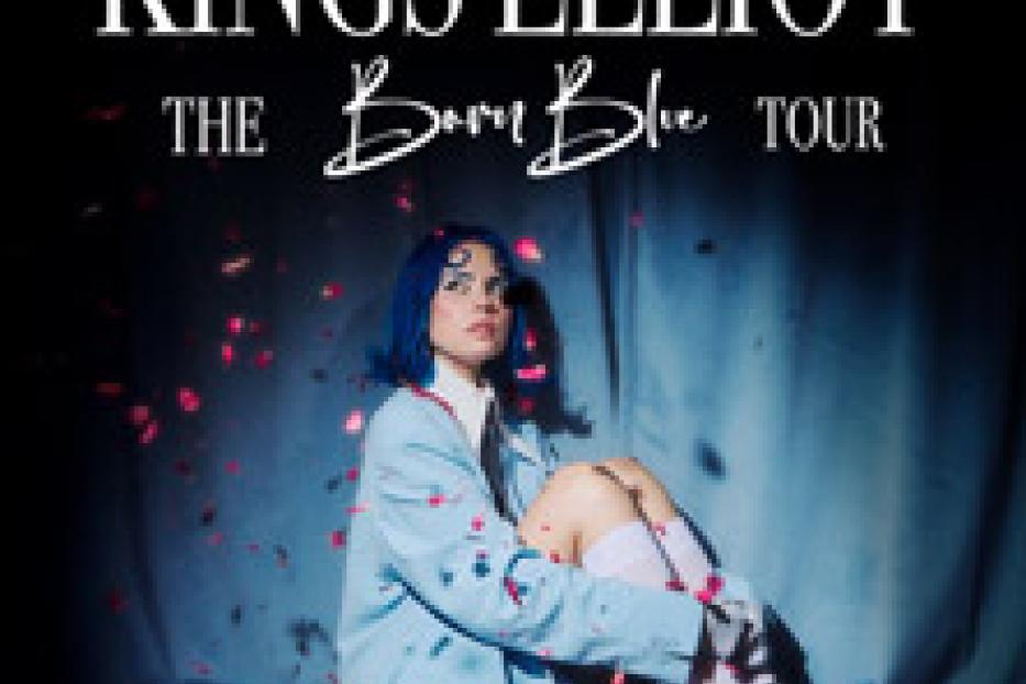 Kings Elliot sitzt vor einem blauen Vorhang, umgeben von Rosenblättern, für ihre „Born Blue Tour“.