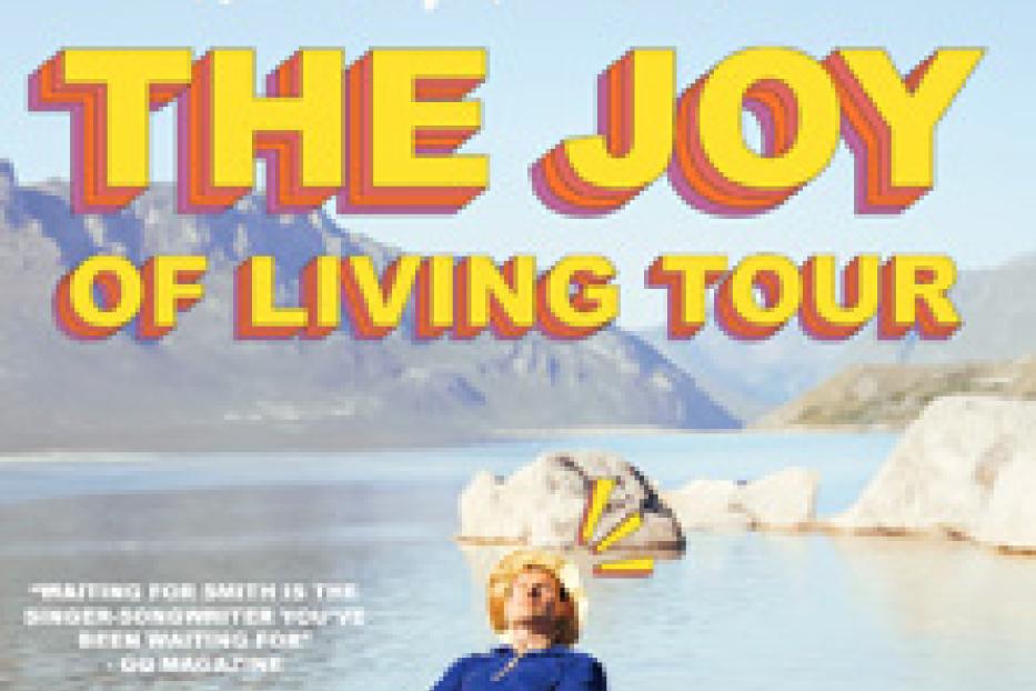 Ein Mann liegt im Wasser vor einer Bergkulisse, bewirbt die „The Joy Of Living Tour“ von Waiting for Smith.