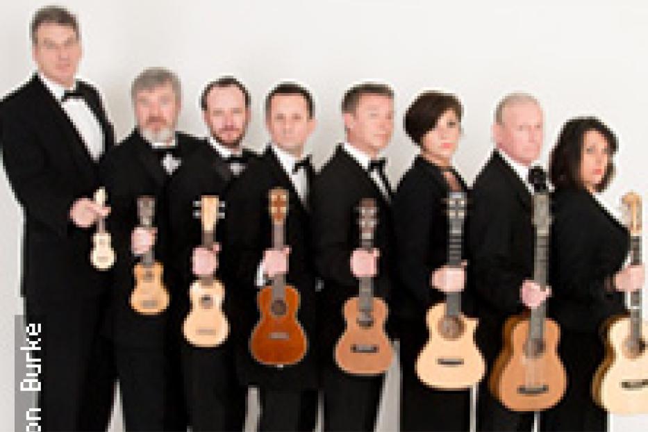 Eine Gruppe von neun Personen in Anzügen hält Ukulelen.