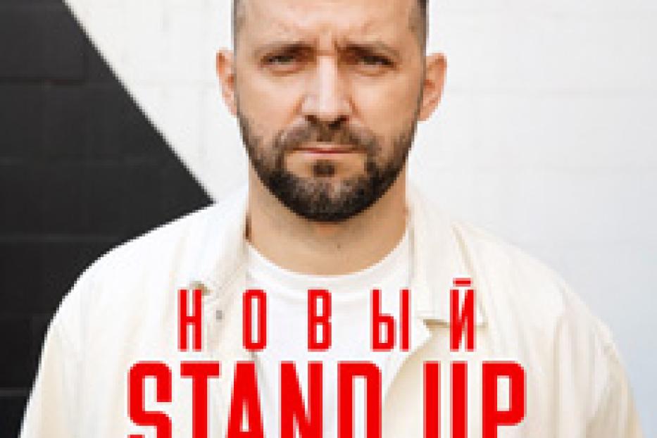 Ein Porträt eines Mannes mit Bart vor einer Wand mit einer roten Aufschrift in kyrillischer Schrift.