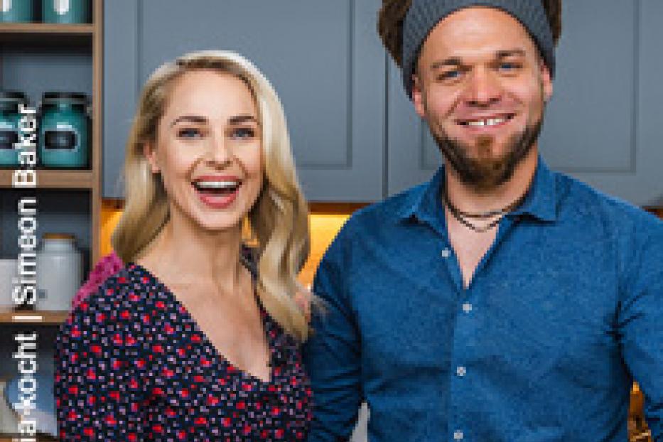 Eine lächelnde Frau und ein lächelnder Mann präsentieren Teller mit Speisen.