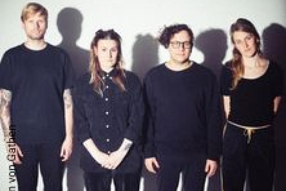 Die Band International Music steht vor einer grauen Wand.