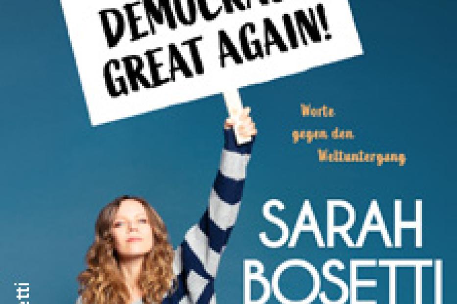 Sarah Bosetti hält ein Schild mit der Aufschrift „Make Democracy Great Again!“ hoch.