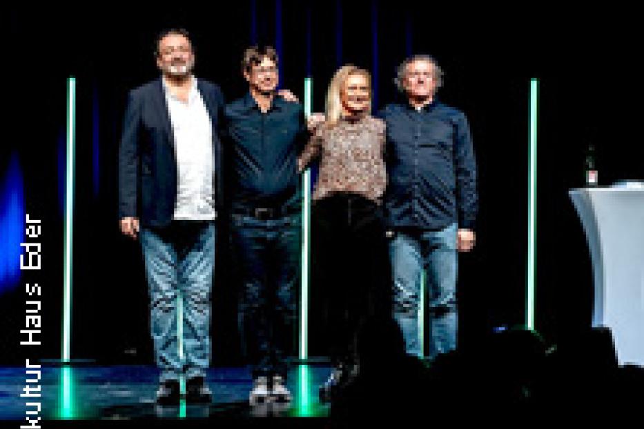 Vier Personen stehen auf einer Bühne vor blauem Hintergrund.