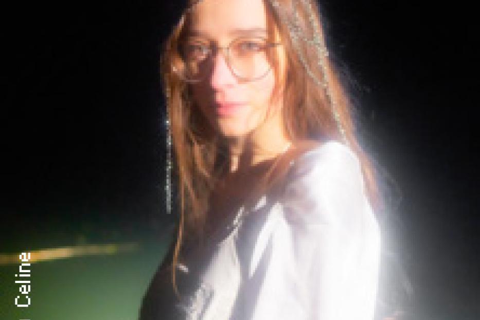 Eine junge Frau mit Brille und Kopfschmuck blickt in die Kamera.