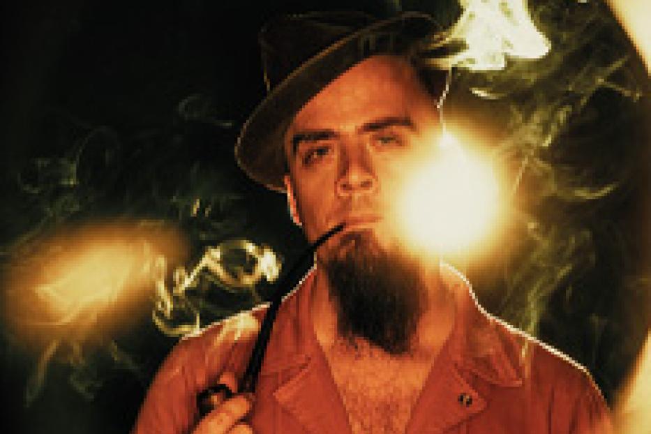 Ein Mann mit Bart und Hut raucht eine Pfeife, umgeben von Rauchschwaden.