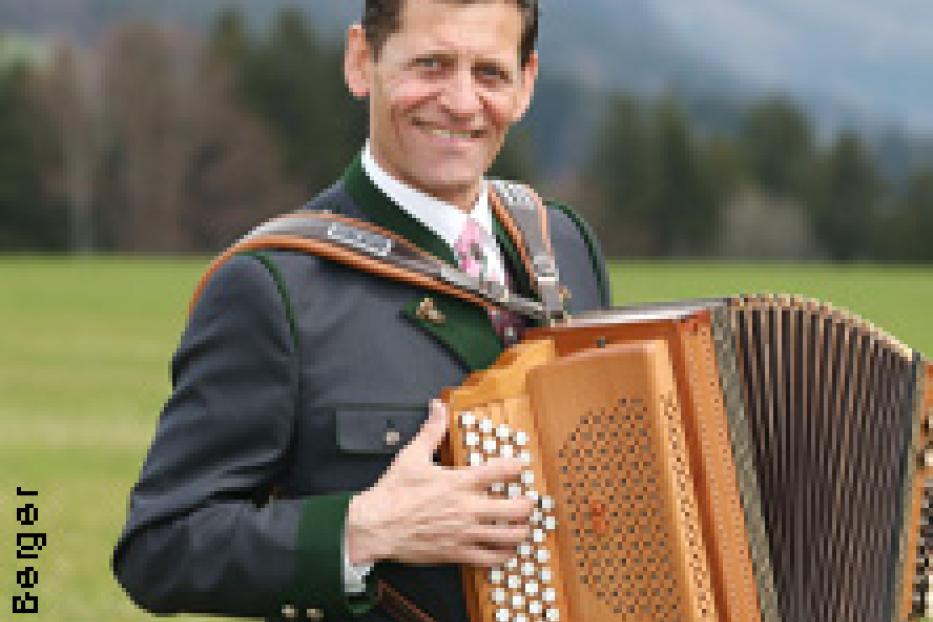 Ein Mann in Tracht hält eine steirische Harmonika in der Hand.